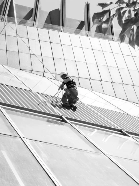 Two workers cleaning windows on a glass building facade using a lift platform, enhancing building aesthetics.